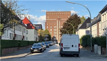 Autos parken in einer Straße. Rechts und links der Straße stehen Mehrfamilienhäuser.