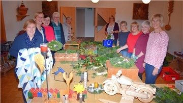 Hier stellen Frauen aus dem Basarteam gerade weihnachtliche Türkränze her. Ein kleiner Ausschnitt aus dem vielfältigen Basarangebot ist im Vordergrund zu sehen.