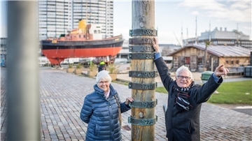 Hier, wo der Sturmflutpfahl unterm Deich steht, war ihre Schiffsausrüstungsfirma: Rolf und Renate Wilhelm haben den Sturmflut-Arbeitsmorgen genau hier miterlebt, als draußen die Weser so hoch stand, wie der Rentner auf der Markierung zeigt. Hier unten wateten sie durch etwa 20 Zentimeter hohe Überschwemmung.
