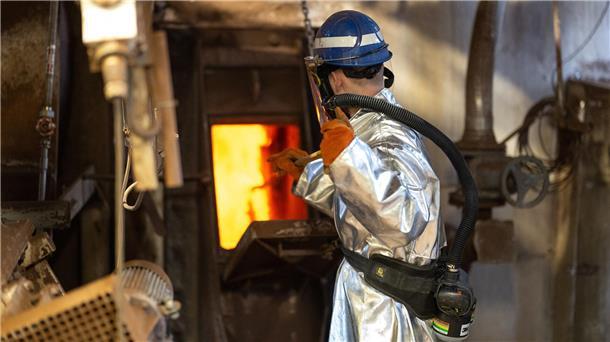 Arbeiter im Hitzeschutzanzug vor Ofen in Metallwerk, Glencore-Standort Nordenham