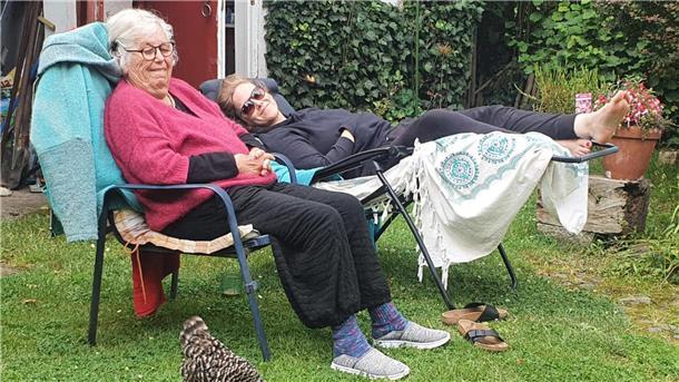 Zwei Frauen in Gartenstühlen davor ein schwarz-weißes Huhn