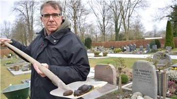 Ein Mann hält auf dem Atenser Friedhof eine Schippe mit Hundekot in die Kamera.