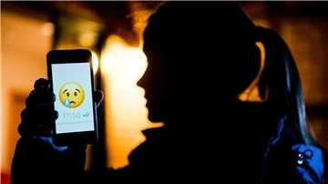 Ein Mädchen hält ein Handy in der Hand. Darauf ist ein trauriger Smiley zu sehen.