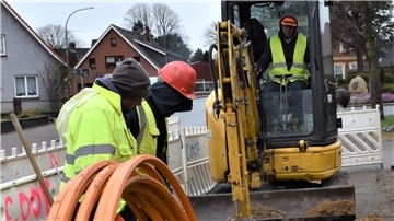 Mehrere Bauarbeiter verlegen ein Glasfaser-Kabel-