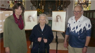 Zwei Frauen und ein Mann stehen vor zwei aufgestellten Fotos