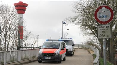 Polizeifahrzeuge auf einer Brücke mit einem Leuchtturm im Hintergrund. Die Ankunft des Atom-Frachters "Pacific Grebe" in Nordenham sorgt für eine erhöhte Polizeipräsenz in der Stadt.