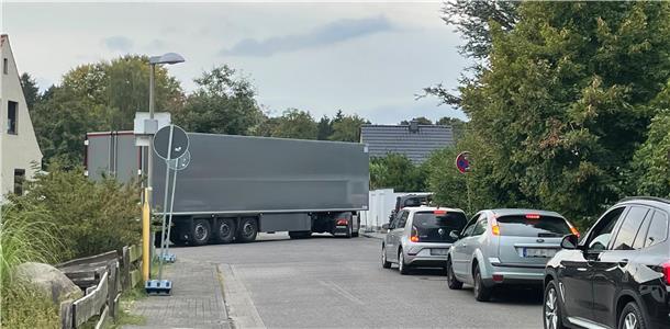 Ein Lkw, der um eine Kurve fahren will. Autos stehen auf der einmündenden Straße und warten.