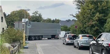Ein Lkw, der um eine Kurve fahren will. Autos stehen auf der einmündenden Straße und warten.