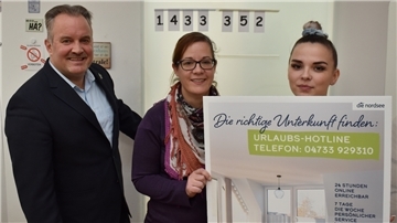 Im Büro der Zimmervermittlung in Burhave mit der aktuellen Umsatzzahl oben an der Tür: Geschäftsführer Robert Kowitz, Leiterin Jana Müller und Mitarbeiterin Kitana Petz  (von links).