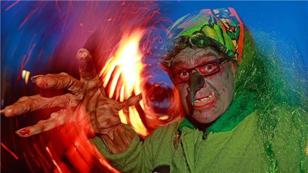 Im Hexenkostüm steht ein Besucher des Walpurgisfestes in Schierke am Feuer.