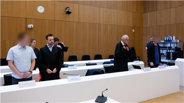 Im Hochsicherheitsgerichtssaal vom Landgericht München II stehen die zwei wegen Mordes angeklagten Männer (l und r) neben ihren Rechtsanwälten.