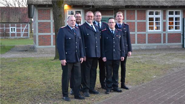 Sechs Feuerwehrleute stehen in festlicher Uniform vor einem norddeutschen Fachwerkhaus.