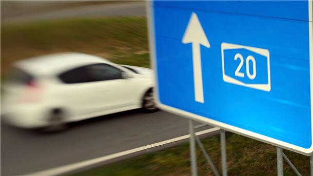 Ein Autobahnschild, an dem ein Auto vorbeifährt. 