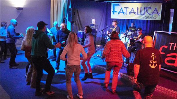 Menschen tanzen im Güterschuppen in Nordenham vor einer Bühne, auf der die Band Fatallica spielt.