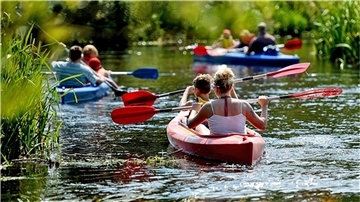 Acht Ausflügler sind in drei Kanus auf einem Fluss unterwegs