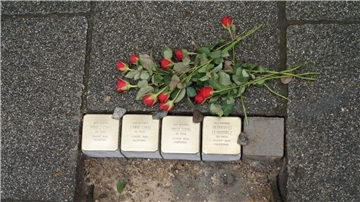 Vier Gedenksteine sind frisch in das Pflaster eines Gehwegs verlegt worden. Darüber liegt ein Blumenstrauß.