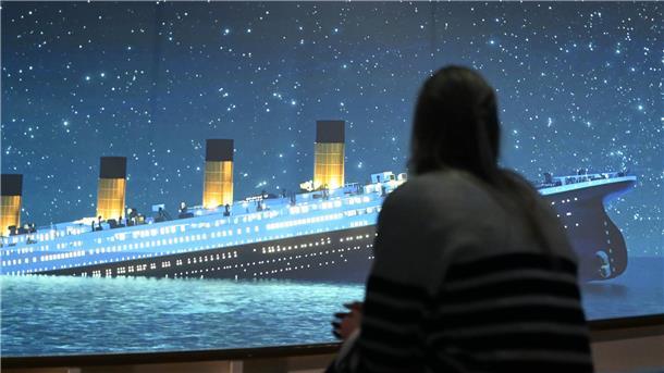 „Titanic“-Erlebnis in Hamburg: Eine Reise in die Vergangenheit Eine Ausstellungsbesucherin ist von hinten zu sehen. Sie sieht auf einer Leinwand die sinkende "Titanic".