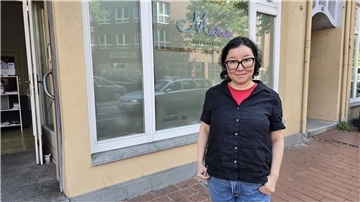 Eine Frau mit schwarzer Leinenbluse und Brille vor einem Schaufenster auf dem "Marie - Beratungstelle" steht.