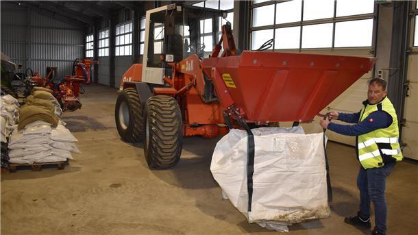 In einer Halle wird eine große Tasche mit Sand befüllt.