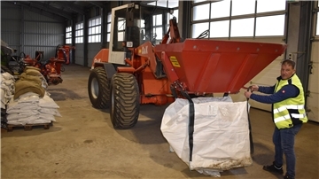 In einer Halle wird eine große Tasche mit Sand befüllt.