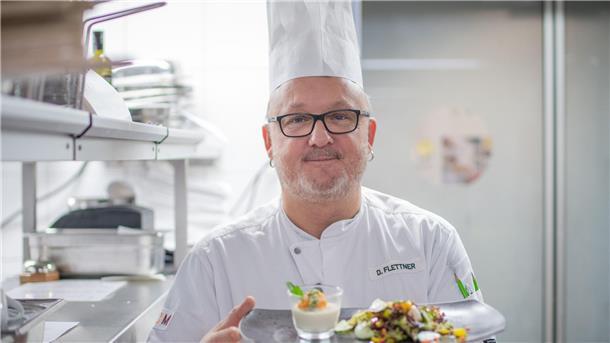 Küchenchef Dominik Flettner aus dem Atlantic Hotel Sail City in Bremerhaven mit Kochmütze und angerichtetem Teller.