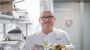 Küchenchef Dominik Flettner aus dem Atlantic Hotel Sail City in Bremerhaven mit Kochmütze und angerichtetem Teller.