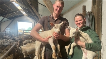 Mann und Frau mit je einem Lamm auf dem Arm im Stall