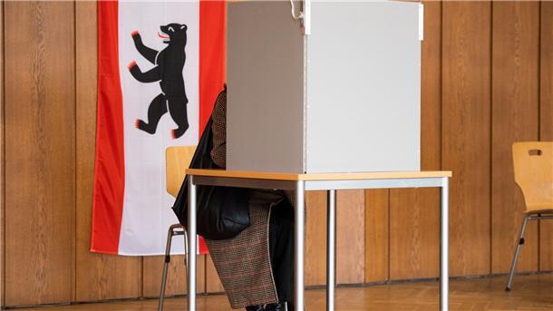 Wiederholungswahl in Berlin: Geringere Beteiligung In einem Wahllokal hängt neben einer Wahlkabine eine Berlin-Flagge.
