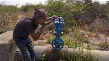 In Indien trinkt ein Mann Wasser aus einer undichten Wasserstelle.
