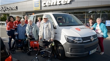 Alte Menschen mit Rollatoren vor einem Einkaufscenter.