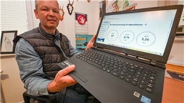 Ein Mann hält einen Laptop in die Kamera