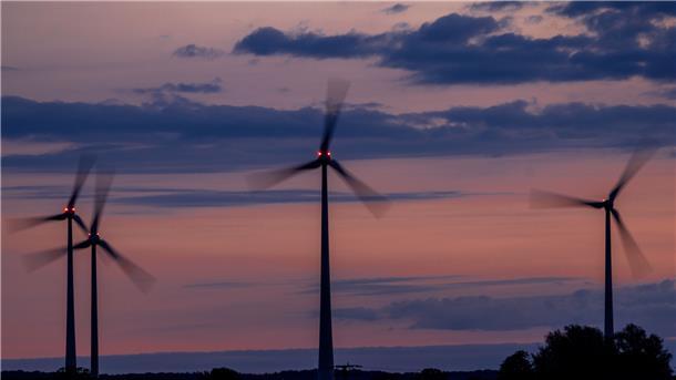 Windräder drehen sich vor Sonnenaufgang und werden von roten Warnleuchten markiert. 