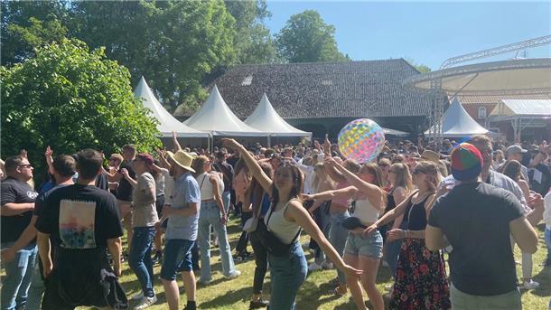 Zahlreiche Menschen tanzen auf einer Wiese.