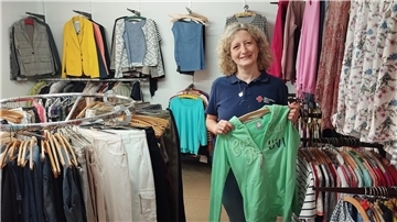 Eine Frau hält ein Kleidungsstück in der Hand. Sie steht in einem Bekleidungsgeschäft.