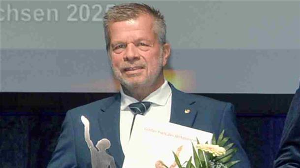 Regionale Unternehmensgruppe unter den besten 28 in Deutschland Ulrich Seier im Anzug bei der Preisverleihung des „Großen Preises des Mittelstandes“. Er hält eine Urkunde, einen Blumenstrauß und eine silberfarbene Trophäe in der Hand.