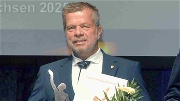 Regionale Unternehmensgruppe unter den besten 28 in Deutschland Ulrich Seier im Anzug bei der Preisverleihung des „Großen Preises des Mittelstandes“. Er hält eine Urkunde, einen Blumenstrauß und eine silberfarbene Trophäe in der Hand.