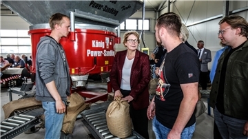 Niedersachsens Innenministerin Daniela Behrens steht mit mehreren Personen vor einer Sandsackfüllmaschine in einer Halle und hält einen gefüllten Sandsack.