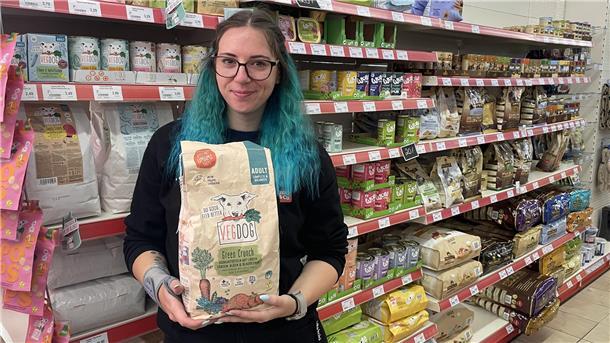 Eine Frau steht vor einem Regal mit Tierfutter. In den Händen hält sie einen Sack Hundefutter.