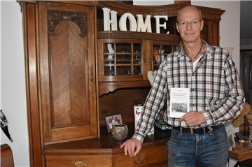 Das Foto zeigt Johann Tomforde in seinem Wohnzimmer mit einem Buch in der Hand. 
