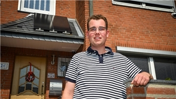 Ein junger Mann vor der Eingangstür zu einem Haus.  