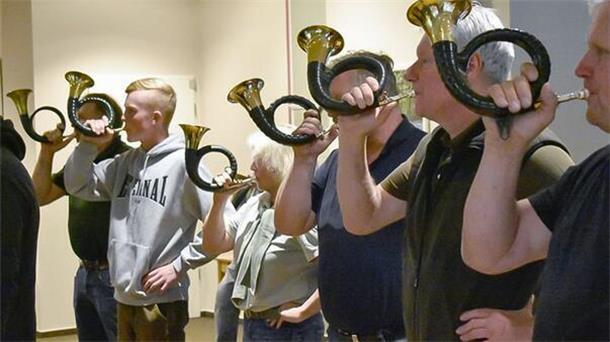 Männer und Frauen blasen in Hörner.