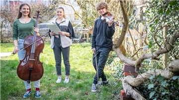 Felicitas Froebe, Aliya Döscher und Jakob Froebe stehen mit ihren Instrumenten in einem Garten.