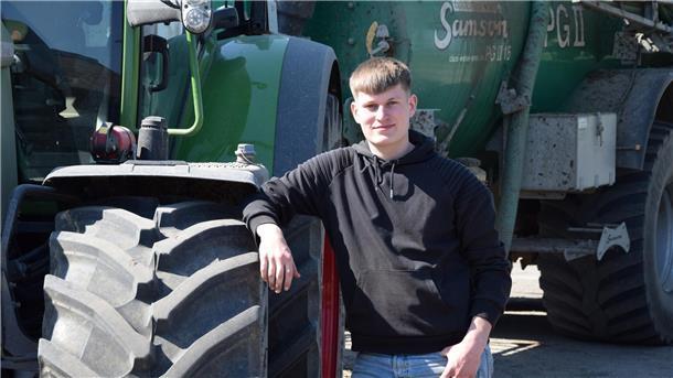 Junger Mann steht neben einem Traktor. 