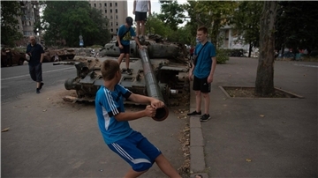 Jungen spielen an einem zerstörten russischen Panzer, der auf einer Straße von Mykolajiw steht.