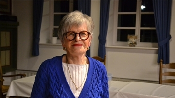 Eine ältere Frau im leuchtend blauen Strickpullover lächelt in die Kamera.