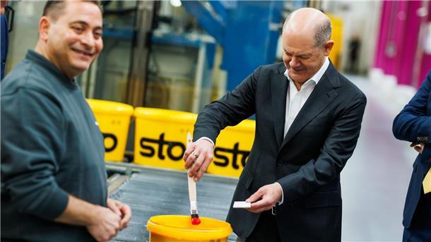 Kanzler Scholz macht beim Baustoffhersteller Sto eine Farbenprobe.