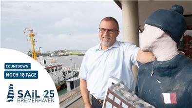 Mann steht neben einer Figur, im Hintergrund ein Schiff