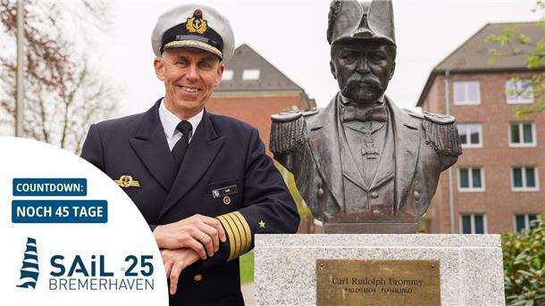 Marine zeigt Flagge bei der Sail: Empfang, Fahrdienst und Karrieretipps Ein Marineoffizier in Uniform steht lächelnd neben einer Büste von Carl Rudolph Brommy; im Vordergrund ein Countdown zur Sail 2025 in Bremerhaven mit „Noch 45 Tage“.
