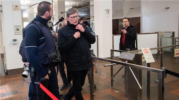 „Kardinal Woelki bitte auf Saal 142!“: Aussage vor Gericht  Kardinal Rainer Maria Woelki wird im Foyer des Kölner Landgerichts von einem Justizbeamten (l) zur Sicherheitsschleuse begleitet.