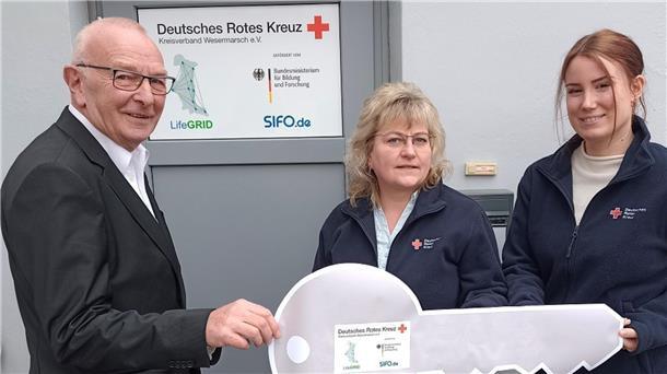 Neue Geschäftsräume für das DRK-LifeGRID-Projekt übergeben Karl-Heinz Röben, Vorsitzender des DRK-Kreisverbandes Wesermarsch, übergibt Kathleen Hirsch und Chariece Atli als Expertin für die Pflege symbolisch den Schlüssel für die neuen Geschäftsräume des DRK-LifeGRID-Teams in der Breiten Straße 104 in Brake.